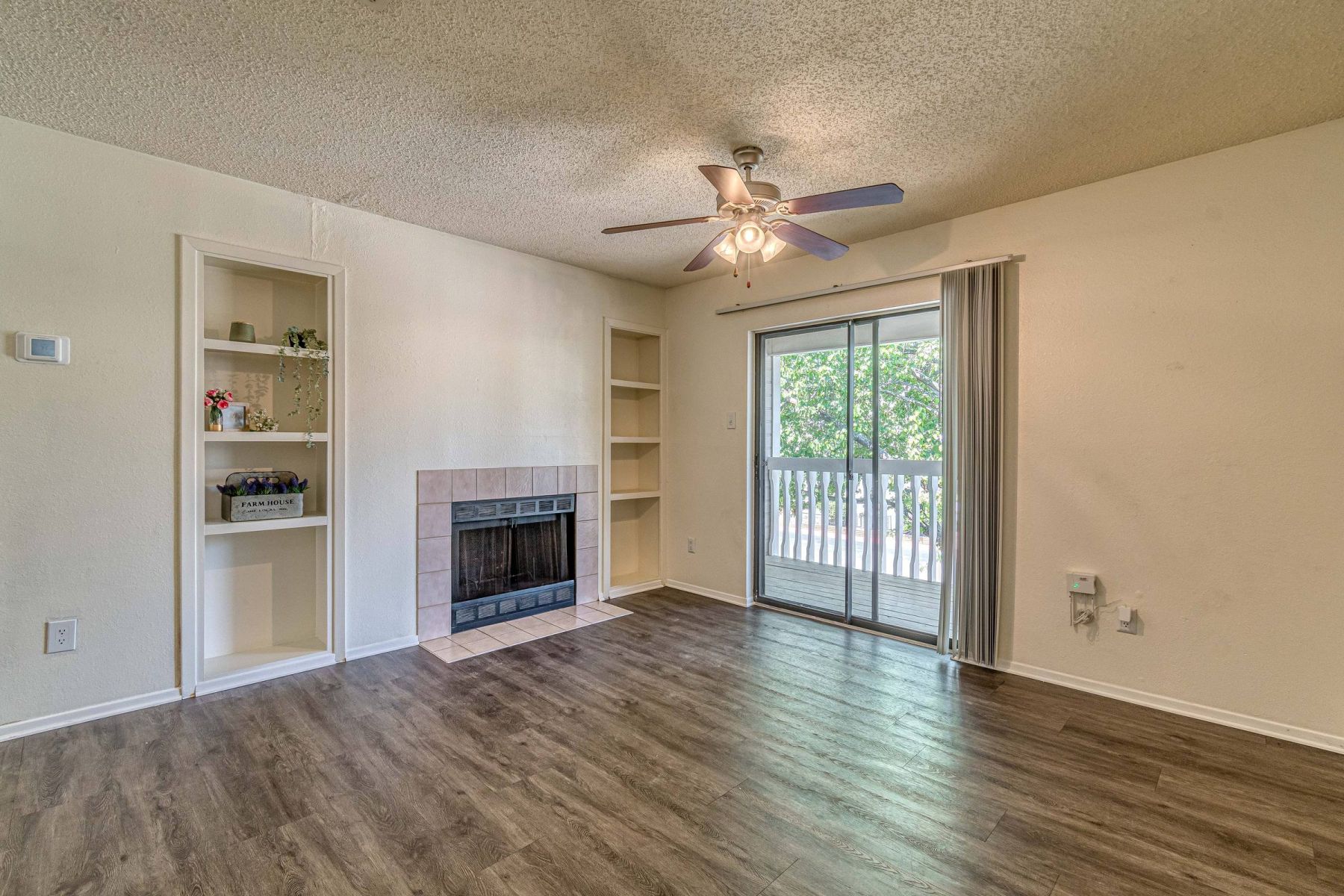 Empty room with wood floors, ceiling fan, and sliding glass door leading to a patio with vertical blinds at Apex West Midown.